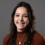 Female veterinarian with long wavy brown hair wearing a brown turtleneck