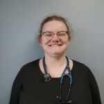Female veterinarian with glasses and dark red hair wearing a black shirt