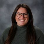 Female veterinarian with long brown hair wearing glasses and a dark green sweater